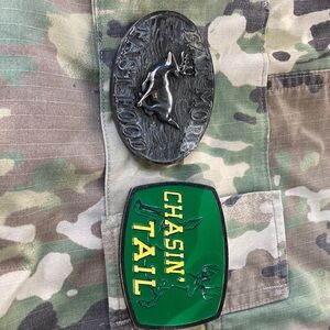 Two belt buckles one says chasing tail other says eat more fast food